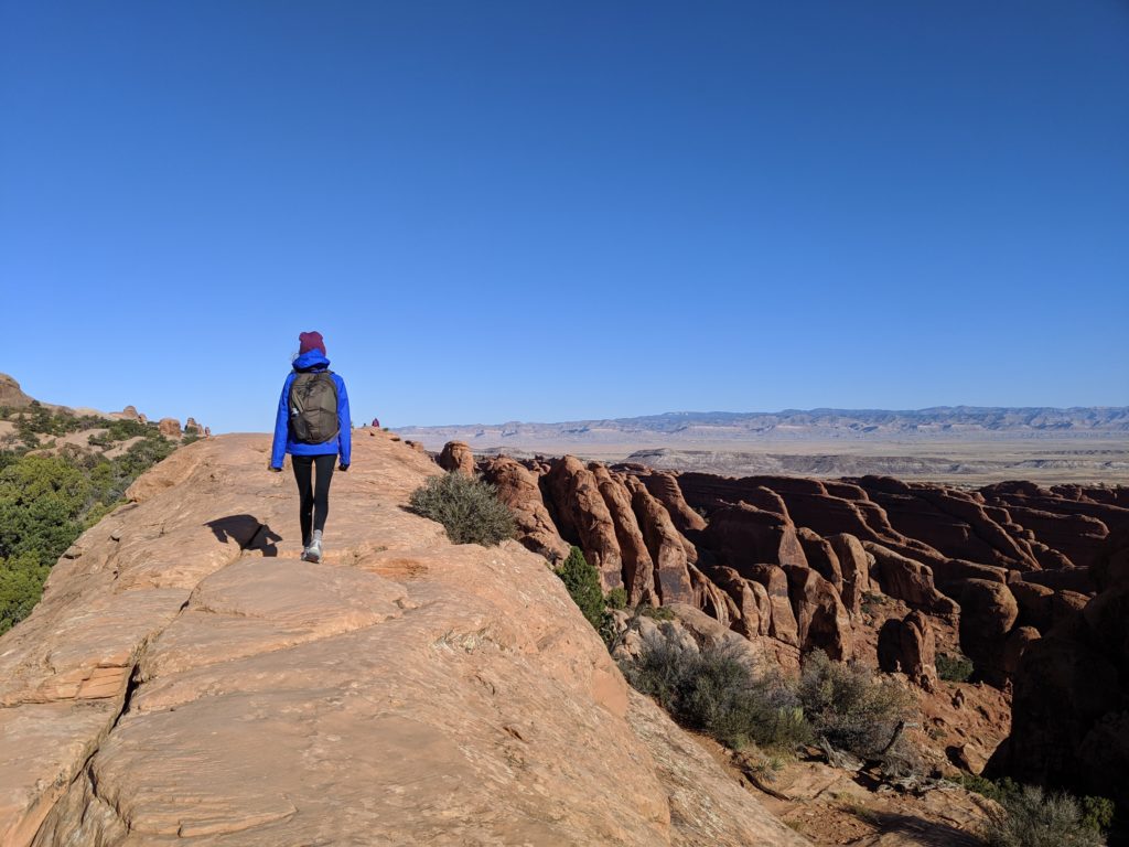 Person walking on top of rock with rocks and sky in background.